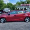 A 2018 Chevrolet Cruze LT Turbo sedan in red is parked at a dealership lot. Other vehicles and a small building displaying the sign Boss Auto Sales can be seen in the background, amid greenery and under a partly cloudy sky.