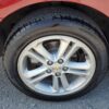 Close-up of a silver alloy wheel with a 5-spoke design on a red 2018 Chevrolet Cruze LT Turbo, showing tire brand and size on the sidewall against gravel pavement.