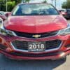 A 2018 Chevrolet Cruze LT Turbo, painted red, is parked in an outdoor lot. The front view shows the Chevrolet emblem on the grille and a Boss Auto license plate. Other vehicles can be seen in the background under a clear sky.