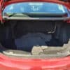 The open trunk of the 2018 Chevrolet Cruze LT Turbo displays a spacious, well-lit cargo area with only a few floor mats. Bright sunlight illuminates the car, with glimpses of the backseat visible through the rear window.