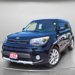 A 2018 Kia Soul EX in black is showcased in a showroom with a neutral gray background, angled to display its front and driver’s side, and featuring a red dealership plate on the front.