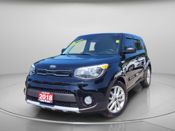 A 2018 Kia Soul EX in black is showcased in a showroom with a neutral gray background, angled to display its front and driver’s side, and featuring a red dealership plate on the front.