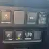 In the 2016 Infiniti QX60 AWD, a close-up of the sleek dark dashboard showcases a car control panel with five buttons: traction control off, an arrow button, ON/OFF Power Door switch, heated steering wheel control, and a circular knob.