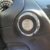 Close-up of the 2016 Infiniti QX60 AWD’s push-to-start button, labeled START STOP ENGINE with an orange indicator above, set in a sleek black dashboard that reflects the SUV’s modern interior design.
