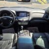 Interior of the 2016 Infiniti QX60 AWD featuring a steering wheel, central display dashboard, gear shift, black leather seats, and dealership floor mats, illuminated by sunlight through the windshield.