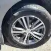 A close-up captures the intricate alloy wheel design of a 2016 Infiniti QX60 AWD, showcasing a clean tire with visible tread patterns mounted on the sleek gray vehicle, all highlighted under bright sunlight.