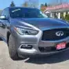 A gray 2016 Infiniti QX60 AWD SUV shines at a used car dealership, certified and surrounded by trees and the Boss Auto Sales building.