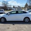 A white Chevrolet Cruze 2LT Turbo, 2017 model sedan, is parked on pavement with houses and cars nearby, under a partly cloudy sky bordered by leafless trees.