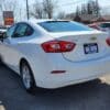 A white 2017 Chevrolet Cruze 2LT Turbo sedan is parked outside in a lot, with a Gas Saver sign on the rear license plate. Other cars and buildings appear under a clear sky in the background.