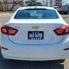 A 2017 Chevrolet Cruze 2LT Turbo in white is parked in a lot, displaying a GAS SAVER sign on the license plate area to promote Boss Auto, with other cars and buildings in the background.