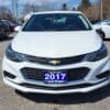 A 2017 Chevrolet Cruze 2LT Turbo sedan with a prominent emblem on the grille is parked in a lot. The license plate reads 2017 Turbo, and additional cars can be seen under the clear sky.
