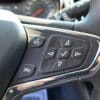 A close-up of the 2017 Chevrolet Cruze 2LT Turbo steering wheel shows control buttons featuring voice command, volume, and navigation icons. A checkmark and arrows are visible, while the dashboard meters are blurred in the background.
