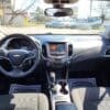 The 2017 Chevrolet Cruze 2LT Turbo boasts a modern interior with its iconic steering wheel logo, sleek dashboard, touchscreen interface, gear shift, and comfy seats. Floor mats saying Your Business is Appreciated are illuminated by sunlight through the windshield.