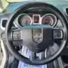 Close-up of the 2015 Dodge Journey SEs black steering wheel, dashboard with two large dials, a digital display, and partial views of the drivers seat and door. A sign says THANK YOU SERVING.