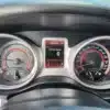 The image depicts the dashboard of a 2015 Dodge Journey SE, highlighting both analog gauges and a digital display. The speedometer reads 0 km/h, with fuel, temperature, and RPM levels shown. The digital screen indicates mileage and prompts to switch to mph.