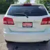 The back view of a 2015 Dodge Journey SE is shown outdoors with a CERTIFIED license plate displaying dealership contact info. Trees and a clear sky enhance the background.