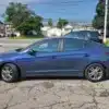 A 2018 Hyundai Elantra Limited is parked on cracked asphalt with trees, houses, and other cars in view under a clear sky.