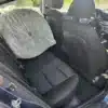 The interior of a 2018 Hyundai Elantra Limited, viewed from outside with the back door open, shows a large plastic-wrapped tire on the back seats. The front seat headrests contrast sharply with the dark upholstery, offering a peek into its blend of practicality and style.