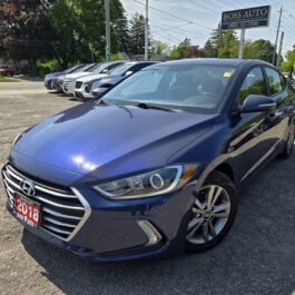 A 2018 Hyundai Elantra Limited is parked at a car dealership lot under sunny skies, with other vehicles and a BOSS AUTO sign visible in the background.