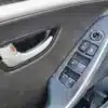 Close-up of a 2014 Hyundai Elantra GT door interior featuring a silver handle, window controls, and side mirror adjustment switch on a dark panel with a sleek, modern design.