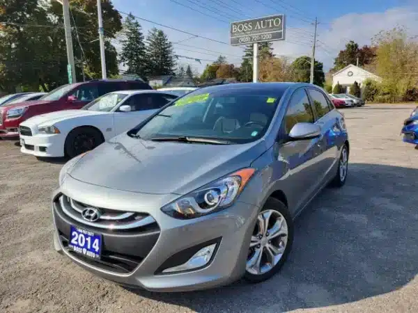 A 2014 Hyundai Elantra GT in silver is parked in a used car lot at Boss Auto, with other cars and a clear blue sky enhancing the charm of the sunny day.