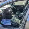 The inside view of the 2014 Hyundai Elantra GT highlights sleek black leather upholstery on the front seats. The dashboard and steering wheel are visible, with a floor mat featuring printed text and foot outlines neatly placed on the drivers side floor.