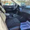 The 2014 Nissan Rogue 2.5 SV interior, seen from the drivers door, features two front seats with dark upholstery, a central console with gear shift, and a dashboard screen. A floor mat reads Your business is appreciated, with other vehicles visible outside.