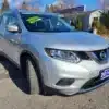 A 2014 Nissan Rogue 2.5 SV SUV in silver is parked in a lot with a Certified sticker on the windshield. A building and trees are visible in the background under a clear blue sky.