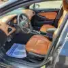 The 2017 Chevrolet Cruze Premier Hatchback interior features orange-brown leather seats, a visible dashboard and steering wheel, and a drivers side floor mat stating Your business is appreciated! The door stands open.