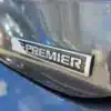 Close-up of a car badge with Premier in silver on a dark gray 2017 Chevrolet Cruze Premier Hatchback, its sleek, reflective surface capturing glimpses of the sky and nearby cars.