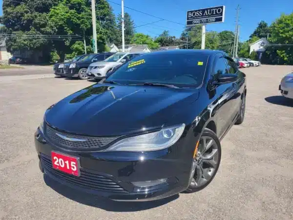 A black 2015 Chrysler 200 S AWD sedan is parked in a car lot with a red license plate. The windshield displays 56,000 km... in yellow writing. Several vehicles and trees are visible in the background, along with a Boss Auto sign above.