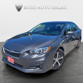 A 2019 Subaru Impreza 2.0i AWD sedan in gray is showcased in a showroom, angled to reveal its front and side, with price details on the windshield and 