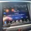 The 2015 Chrysler 200 S AWD dashboard shows a radio tuned to 94.9 FM, playing I Hear You Calling by GOB at 10:33, with AWD control icons organized below.