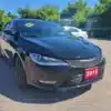 A sleek black 2015 Chrysler 200 S AWD sedan, adorned with a Certified sticker on the windshield, is parked amidst lush green trees on this sunny day.