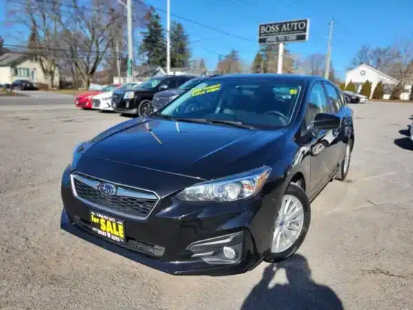 A sleek 2017 Subaru Impreza Premium HB with a For Sale sign is parked on a lot. A sticker reveals its from 2019. Other cars and trees are nearby, alongside a prominent BOSS AUTO sign.