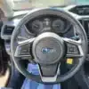 A close-up of the 2017 Subaru Impreza Premium HB interior highlights the Subaru steering wheel with control buttons, a dashboard with gauges and a digital screen, an open door, and a console equipped with climate and audio controls, all showcasing its sleek design.
