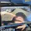 The backup camera display of the 2017 Subaru Impreza Premium HB reveals cars parked on both sides of a lot, with red, yellow, and green guidelines indicating obstacle proximity. It also features the text, Check Surroundings Before Backing Up.