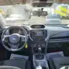 Interior view of a 2017 Subaru Impreza Premium HB showing the steering wheel, dashboard with a touchscreen display, gear shift, and front seats. A decal is visible on the windshield, with several cars in the parking lot beyond.