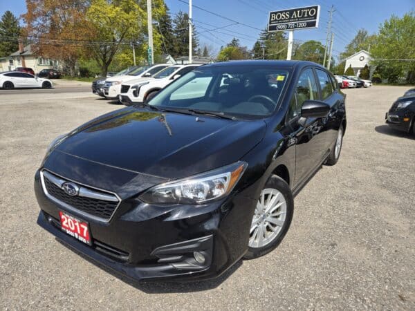 A 2017 Subaru Impreza Premium HB is parked at a dealership under a BOSS AUTO sign, with other cars and green trees in the background on a sunny day.
