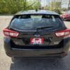 A black 2017 Subaru Impreza Premium HB is parked in a lot, viewed from behind with a red 4x4 BOSS AUTO dealer plate. Other cars and trees are visible in the background.
