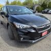 A 2017 Subaru Impreza Premium HB in black is parked in a lot with its front wheels turned outward, with other vehicles and a building visible in the background.