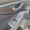 Close-up of a 2017 Subaru Impreza Premium HB interior driver-side door panel, showing the door handle, power window controls, lock, and mirror adjustment buttons with the door partially open.