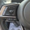 Close-up of a 2017 Subaru Impreza Premium HB steering wheel showing buttons for volume, source, info, phone, and voice commands, with part of the car’s logo visible on the right.
