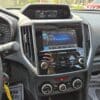 Dashboard of a 2017 Subaru Impreza Premium HB with the infotainment screen on a SiriusXM station, the car in park, sunlight streaming in, and parts of the steering wheel plus climate controls visible.