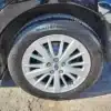 Close-up of a black vehicles car tire and wheel. The tire, a Continental ProContact, is on a five-spoke design wheel. Dirt ground hints at rugged terrains tackled by the 2017 Subaru Impreza Premium HB. Blurred in the background are parts of other vehicles.