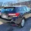 A 2017 Subaru Impreza Premium HB in black is parked outdoors. Its model badge and license plate area are visible at the rear with other vehicles and bare trees nearby under a clear blue sky.