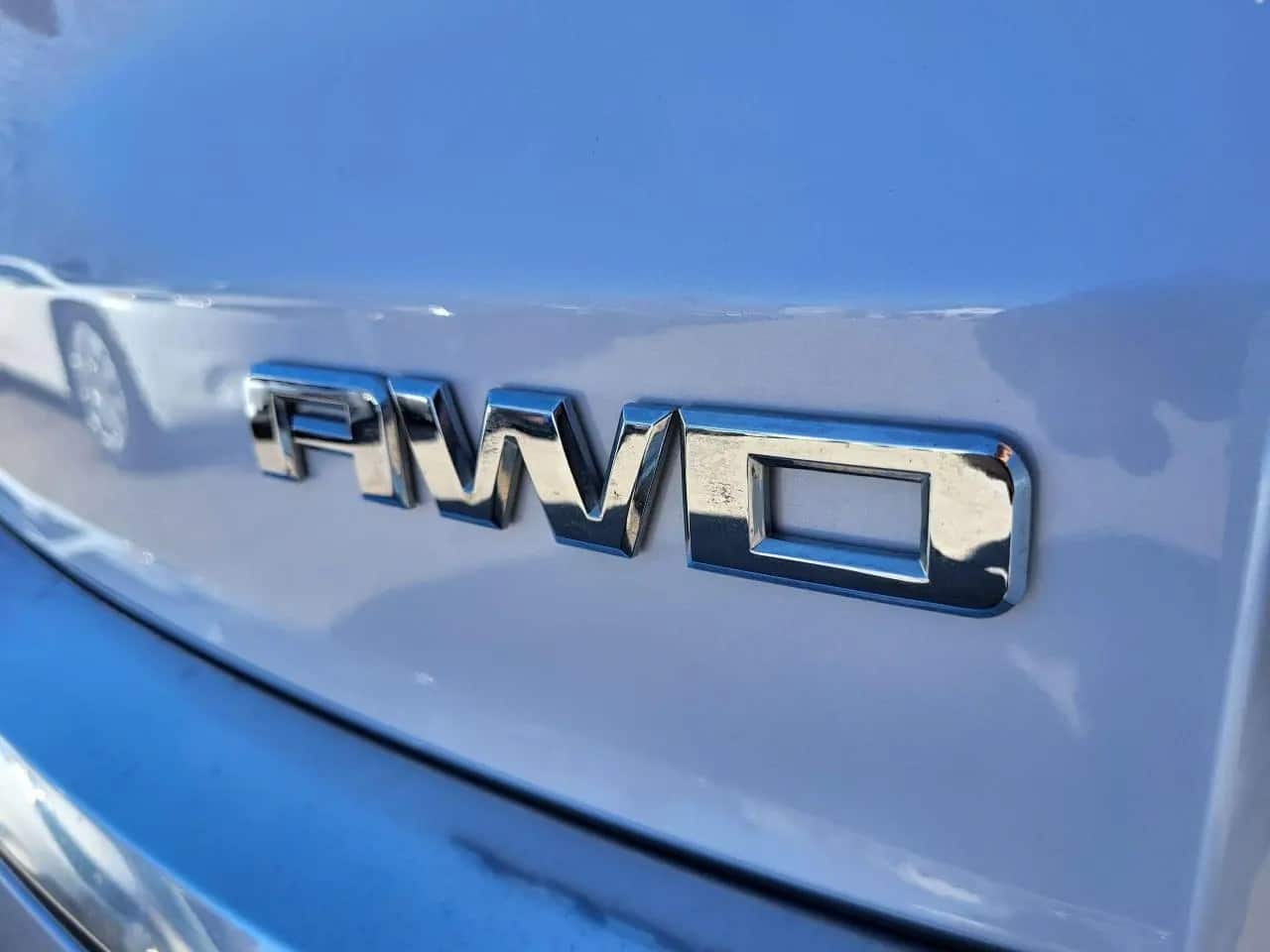Close-up of a shiny silver “AWD” emblem on the back of a light blue 2016 GMC Acadia Denali, with part of another vehicle blurred in the background.