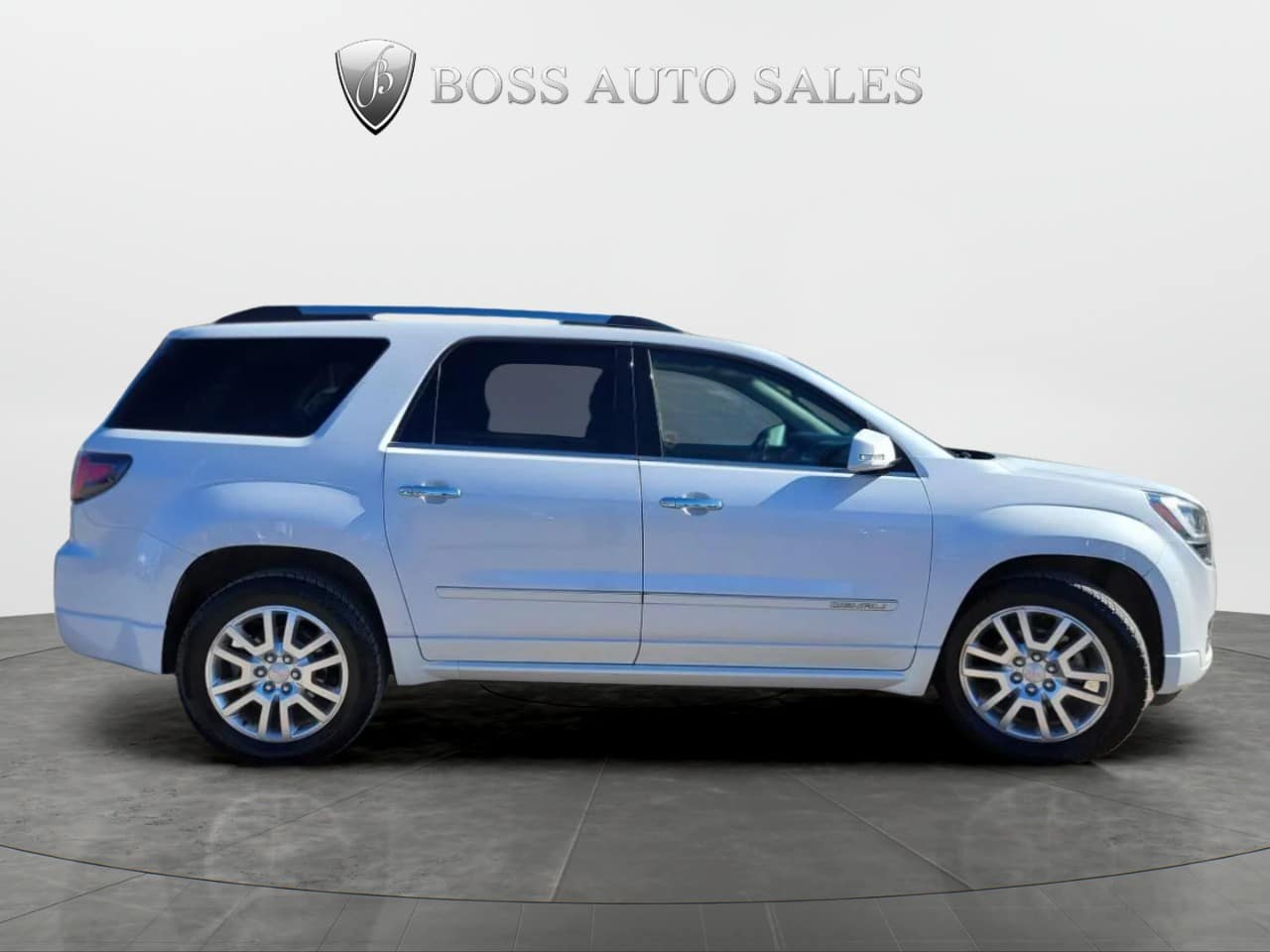 A side profile of the 2016 GMC Acadia Denali AWD is displayed on a turntable platform with the Boss Auto Sales logo and text above, set against a plain neutral background.