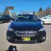 A sleek 2017 Subaru Impreza Premium HB sits proudly in the dealership lot with a For Sale sign on its windshield. Surrounded by other cars under a pristine blue sky, this premium black vehicle beckons potential owners with its alluring presence.