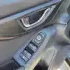 A close-up of the interior door of a 2017 Subaru Impreza Premium HB highlights a chrome handle, a button panel for window and side mirror controls, and a carbon fiber textured surface. The door is slightly ajar.